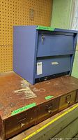 Blue wood cabinet with lock and key on top, sitting on a four-drawer wooden cabinet with visible wear and metal knobs.