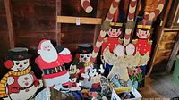 Group view of wood cut out Christmas decorations including Santa, snowmen, Mickey Mouse figures, angels, nutcrackers, and candy canes arranged in a rustic setting
