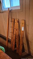 Photo showing four wooden coat hook boards and one long wooden railing board leaning against a paneled wall under a window.