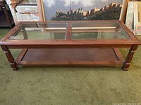 Front view of wooden coffee table with dual glass panels on top and woven bottom shelf, standing on carpet.