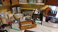 Wide view showing assortment of vintage kitchen items on countertop including metal breadbox, Betty Crocker toaster, baking mold, spice rack, salad spinner, glass jar with contents, white canisters, and small clock.