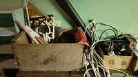 Photo showing a wooden box with various household items, extension cords, and cardboard boxes with power outlets and other small items next to it.