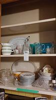 Two shelves filled with various kitchen items including plates, pitchers, glass measuring cups, salt and pepper shakers, and bowls.
