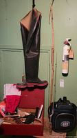 Photo showing black rubber leg waders hanging on wall next to a red metal box with assorted fishing gear, against a green wall.