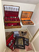 Wooden storage boxes containing Rogers Service Plate flatware set with knives, forks, and spoons, plus assorted stainless steel flatware sets and basket with various utensils displayed.