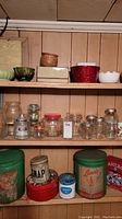 Photo showing shelves with clear glass jars and bottles of varied sizes, planter pots and multiple vintage tins including floral and green tins.