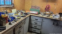 Wide angle of hardware workbench with scattered tools including screwdrivers, hammers, bolt cutters, and various fasteners near a pegboard