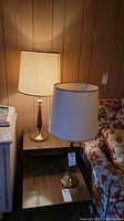 Two retro lamps standing on a wooden side table next to a floral fabric couch, showing overall look and size.