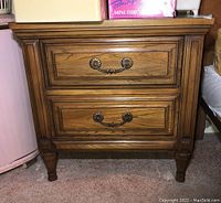Front view of the vintage Malcolm wood bedside table showing two drawers with decorative metal handles.