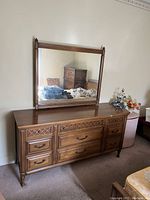 Front view of dresser with nine drawers and matching mirror reflecting room interior.