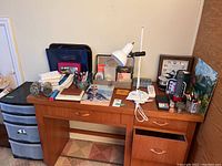Full view of wooden office desk with office supplies on top including lamp, clocks, documents, pencil sharpeners, and calculator