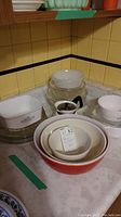 Photo showing assortment of Pyrex, Corningware dishes and bowls on kitchen counter, highlighting nested Pyrex mixing bowls and Corningware pie plates