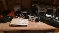 Lot of vintage radios and cassette players on shelf including Whisper 2000, Yorx, Citizen tape deck, and Casio clock.
