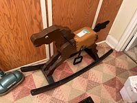 Full side view of the brown wooden rocking horse with black curved rockers and tan vinyl saddle with metal stirrups.