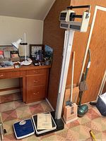 Photo showing two bathroom scales on the floor near a wooden desk, with a tall Sunbeam balance beam physician scale standing behind them against a brown wall