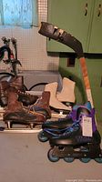 Vintage men's ice skates, white figure skates, Titan inline rollerblades, and wooden hockey stick