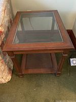 Wood frame side table with glass top and lower shelf, showing front angle against wall.