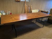 Long wood table shown from side angle in basement room with carpet and other furniture