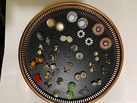 Overview of 34 sets of assorted clip-on and screw-on earrings arranged on a round tray, showing variety in style, color, and material.