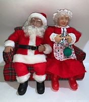 Santa and Mrs. Claus sitting on a plaid loveseat, full view showing attire and seating.