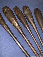 Side view of six wood-handled screwdrivers laid out, showing handles and shafts with wear.