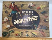 Top view of the closed wooden kit box with colorful printed lid featuring a man fishing and multiple fly patterns