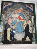 Closeup of 3D molded religious scene inside the picture box showing Madonna holding Child Jesus, flanked by two kneeling saints, with ornate decorative painted frame and inscription 'The Holy Rosary'.
