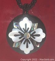 Close-up of the round black pendant displaying white mother of pearl floral inlay with abalone shell accents.