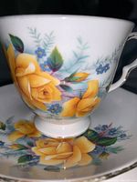 Tea cup and saucer set showing detailed yellow rose and blue flower design with gold trim