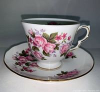 Side view of Queen Anne porcelain teacup showing pink rose floral design and gold trim on handle and base.