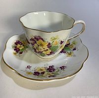 Side angle showing the floral teacup on matching saucer with gold scalloped rims and floral decoration.