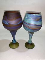 Two hand-blown swirl glass wine goblets, colors purple, blue, brown and green with swirl patterns, 8 inches tall