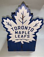 Front view of the wooden bottle holder shaped like a maple leaf, painted in blue and white with Toronto Maple Leafs text.