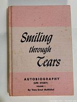 Front cover photo of 'Smiling Through Tears' autobiography book showing pink and cream colored hardcover with title and author name.