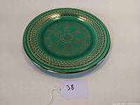 Green ceramic plate with gold woven pattern on outer rim, the plate sits on a white surface with a tag marked '38' nearby.