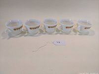 Five white milk glass teacups with golden butterfly design arranged in a row, showing front sides.