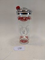 Front view of cocktail shaker displaying the colorful applied designs and chrome lid with red knob