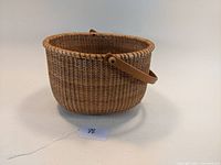 Front angle view of the handwoven Nantucket style basket with wooden swing handle on a plain background.