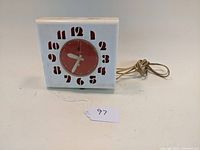 Front view of square white electric kitchen wall clock with red Art Deco numbers and central dial showing time 7:38:00.