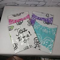 Four packaged tea towels laid out flat showing colorful borders and tea-themed illustrations