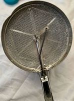 Top-down photo of vintage metal flour sifter mesh part and handle.