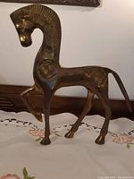 Solid brass horse figurine shown from side angle, highlighting the detailed patterns on the horse's body and the raised front leg.