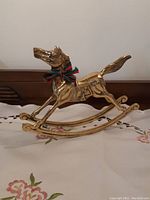 Front angle of brass rocking horse Christmas decor on a cloth surface, showing details of horse's face, saddle, and rocking base.