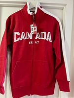 Front view of red fleece jacket with white stripes on sleeves and 'CANADA 1867' embroidery on front.
