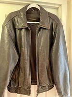Front view of chocolate brown leather jacket on hanger, showing classic collar, front zipper, and elastic waistband