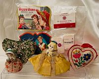 Collection of sewing items including two porcelain-faced pin cushion dolls, heart-shaped embroidered pin cushions, needle books, and travel sewing kits