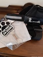 Photo showing XL adjustable black dog harness with reflective strip and Pecute brand logo, nylon chew toy in transparent plastic shaped like a bone, and paw print magnet with 'Fur Kids On Board' text.