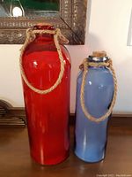 Front view showing the red and blue glass bottle lamps standing upright with visible cork stoppers and rope handles.