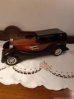 Side view of Heritage Mint wooden collectible car showing streamlined vintage body with black painted roof and fenders, natural polished wooden doors and side panels, and silver-tone accents.
