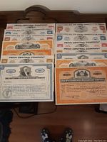 Top-down view showing a spread of fourteen various vintage railroad stock certificates from Pennsylvania and New York companies, placed on a wooden surface.